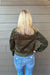 Woman wearing Liverpool Collared Bomber Jacket In Hunter Green with jeans on a dark wood background.