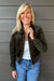 Woman wearing Liverpool Collared Bomber Jacket In Hunter Green with jeans on a dark wood background.
