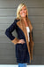 Woman wearing Liverpool Sherpa Notch Collar Jacket In Cinder Bloom with blue jeans on a dark wood background.
