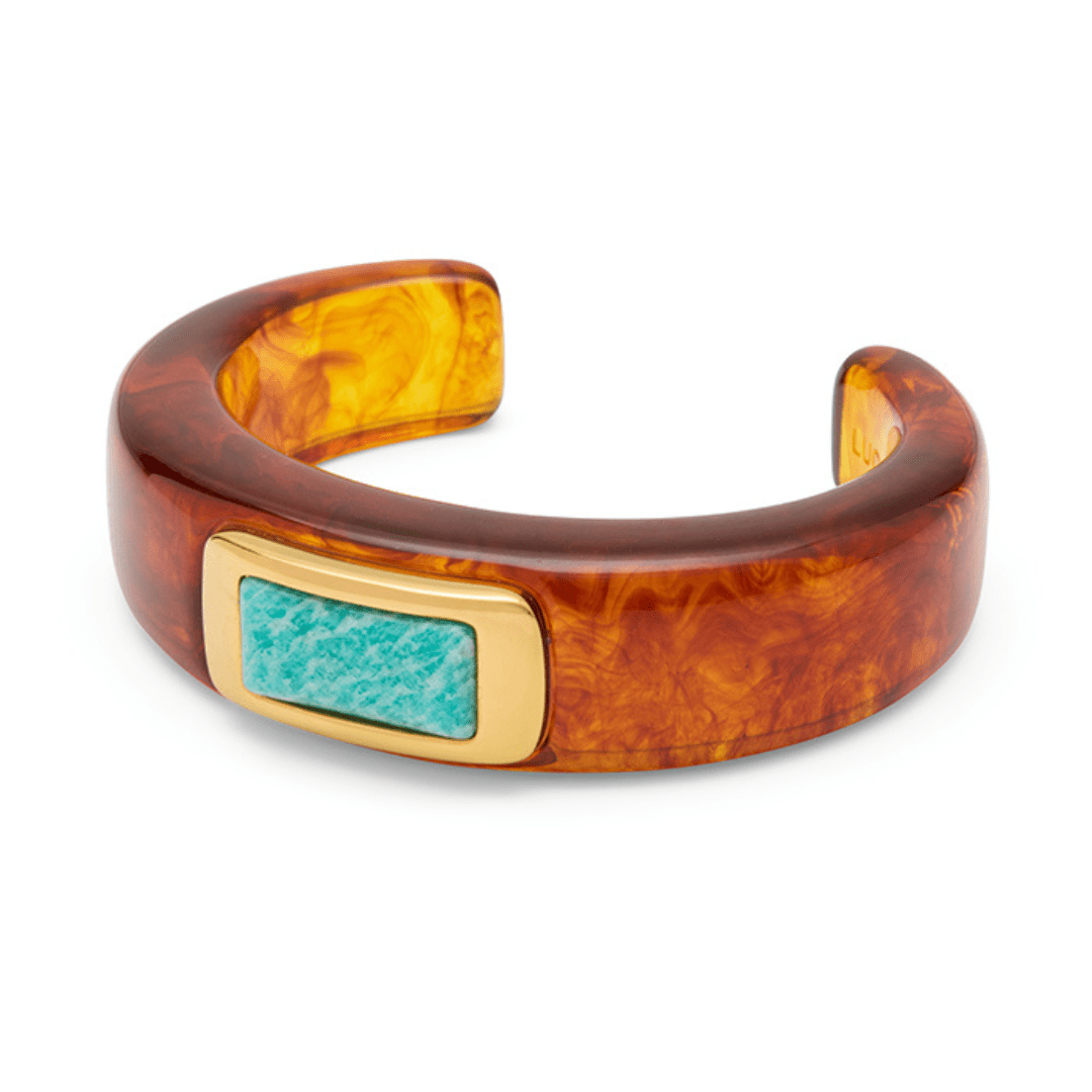 A wide cuff bracelet made of glossy amber-brown marbled resin, featuring a rectangular turquoise inlay surrounded by a gold-tone border, shown on a plain white background.