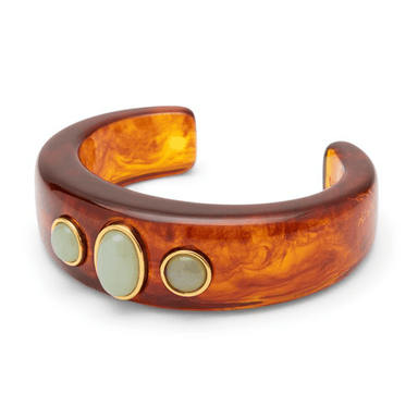 A thick open cuff bracelet made of glossy amber-brown marbled resin, decorated with three oval pale green stones set in gold-tone bezels, shown on a plain white background.