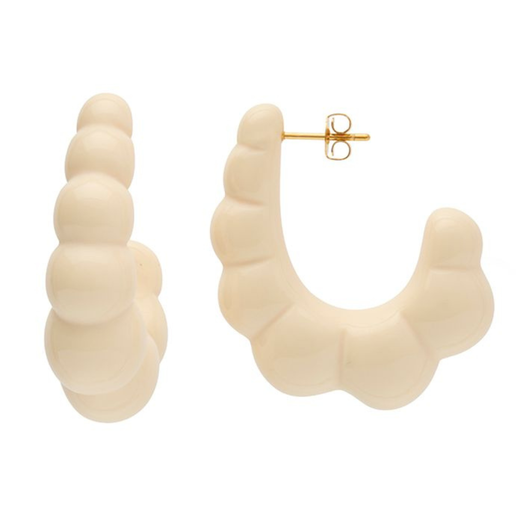 A pair of sculptural, tooth-shaped hoop earrings in a glossy off-white finish, with one earring shown from the front and the other from the side to reveal the gold post and butterfly back.