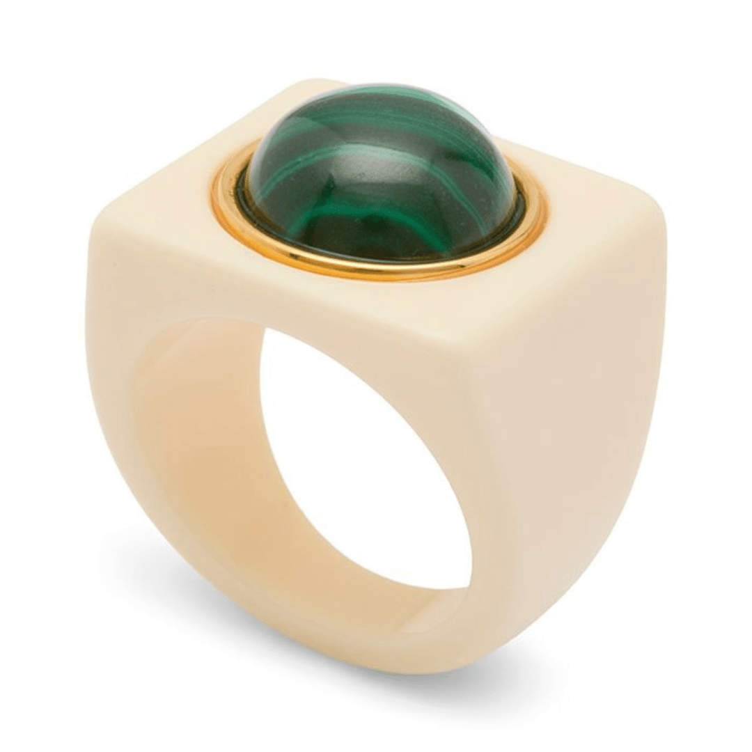 A modern statement ring featuring a matte cream-colored square bezel with a large, polished green malachite cabochon and a thin gold bezel setting, shown on a white background.