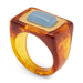 A statement ring featuring a thick, square-shaped translucent tortoiseshell band in amber and orange tones, a polished gold-plated bezel, and a smooth, light blue cabochon gemstone in the center, set against a plain white background.