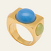 A gold signet-style ring featuring a large, smooth oval blue cabochon on the top and a smaller oval light green cabochon on the side, set against a solid off-white background.