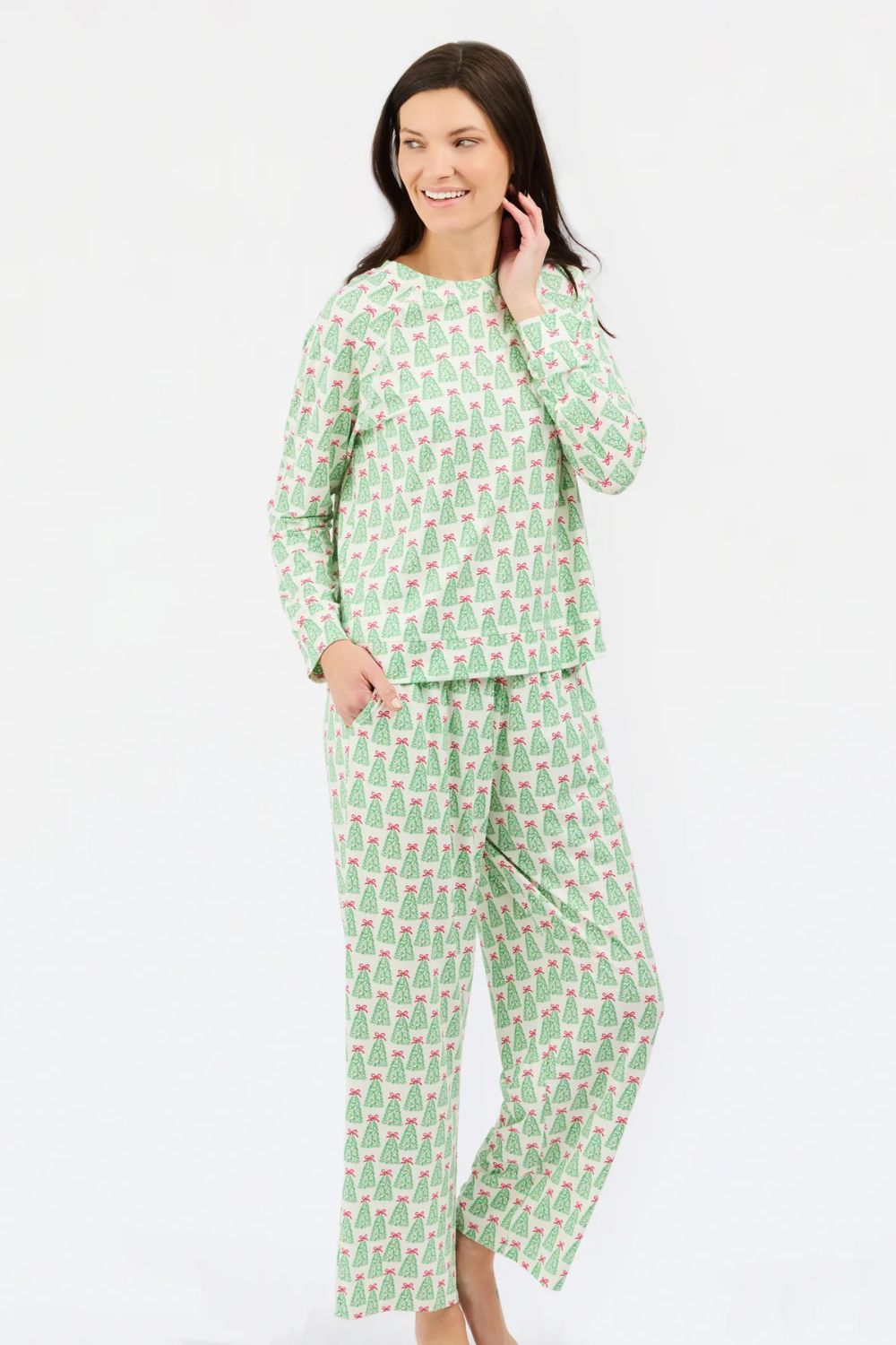 A woman modeling a two-piece long-sleeve pajama set with an all-over green and pink pattern, photographed against a plain white studio background.