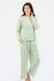 A woman modeling a two-piece long-sleeve pajama set with an all-over green and pink pattern, photographed against a plain white studio background.