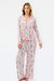 A woman modeling a two-piece long-sleeve pajama set with a pink and green tropical print on a white background, photographed against a plain white studio backdrop.