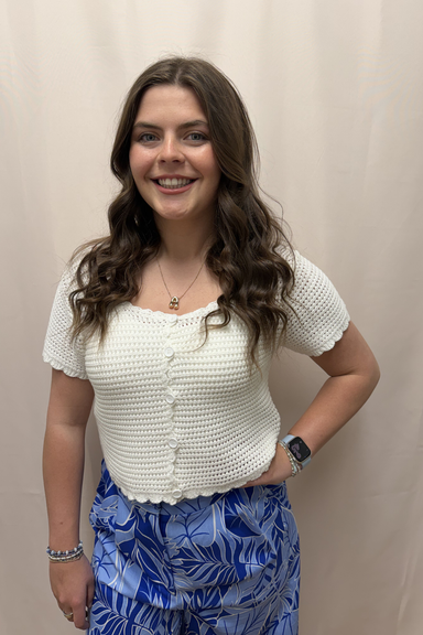 Woman wearing a white textured top and blue patterned pants against a beige background