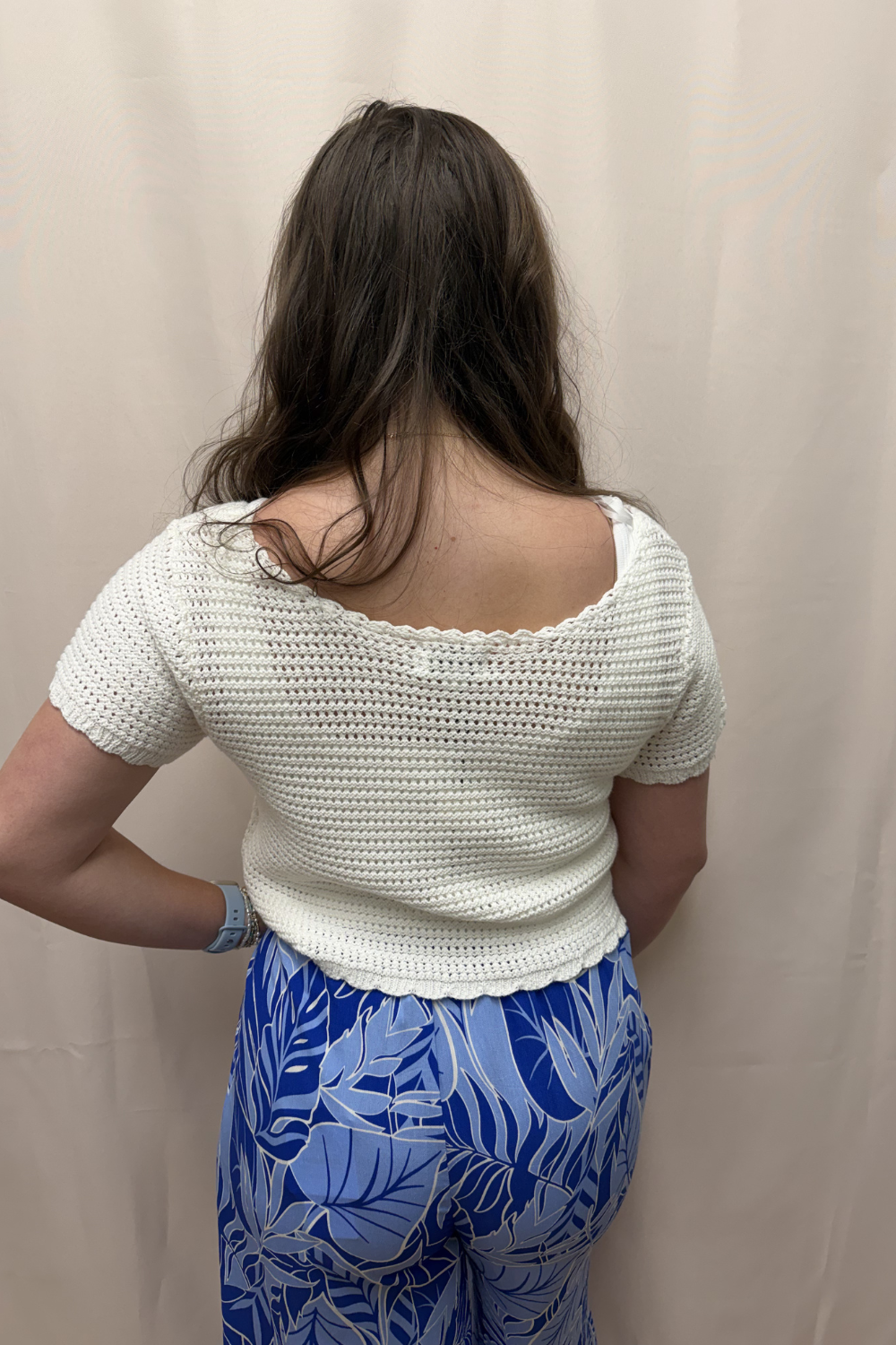 Person wearing a white crochet top and blue patterned pants against a beige background