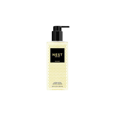 A bottle of NEST London Holiday Hand & Foot Lotion in a clear rectangular bottle showing a pale yellow liquid, with a black pump dispenser and a black label featuring gold lettering.