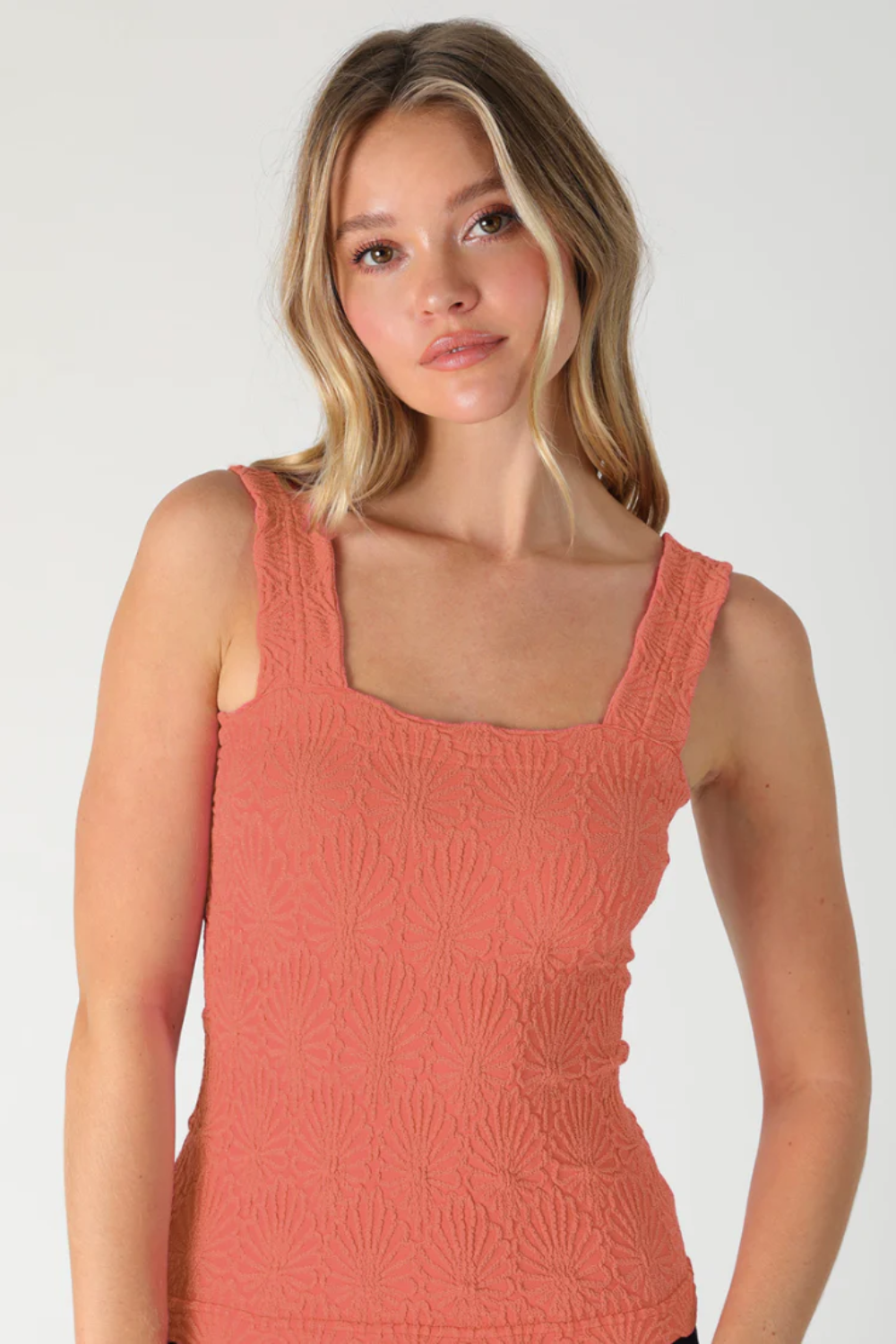 Woman wearing a coral tank top against a plain background