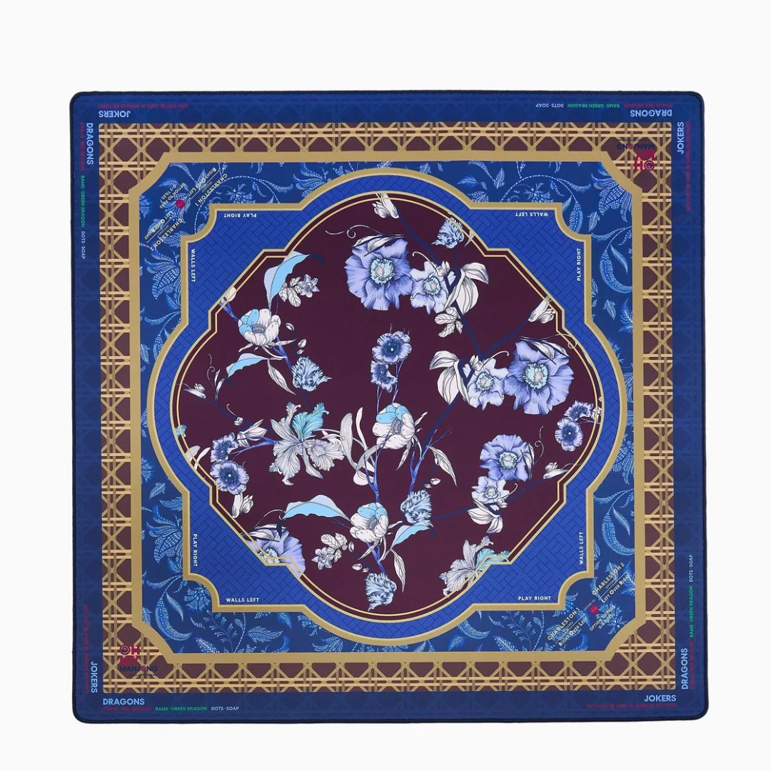 A square silk scarf from the brand Sable des Arts, featuring an intricate floral design. The color palette consists of a deep royal blue border, a gold geometric frame, a central dark plum purple section, and light blue and white floral motifs.