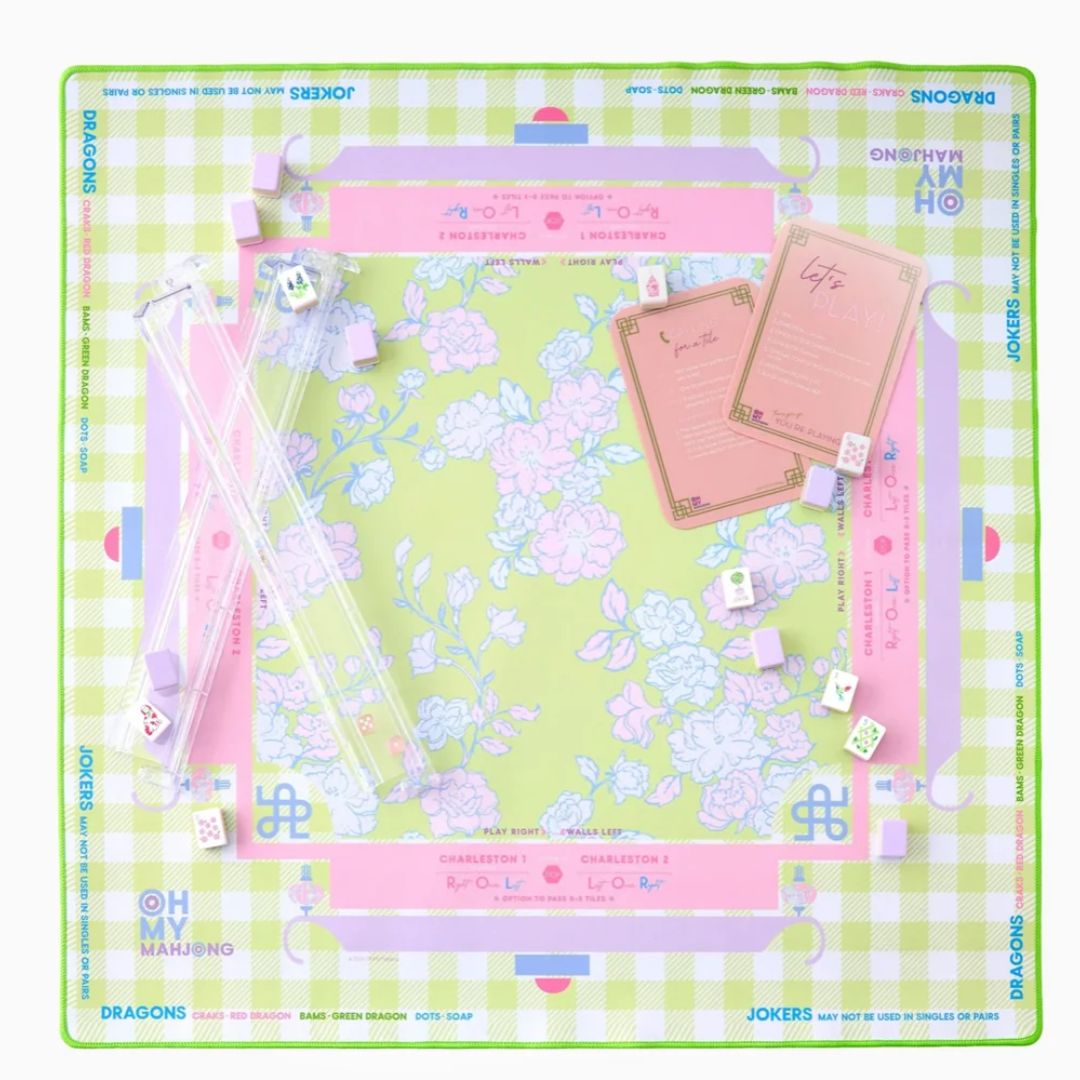 A square board game set featuring a pastel green and pink gingham border, a central floral board with pink and blue illustrations, clear acrylic game pieces, cards, and dice. The brand name 'JOKERS' is visible around the outer border.