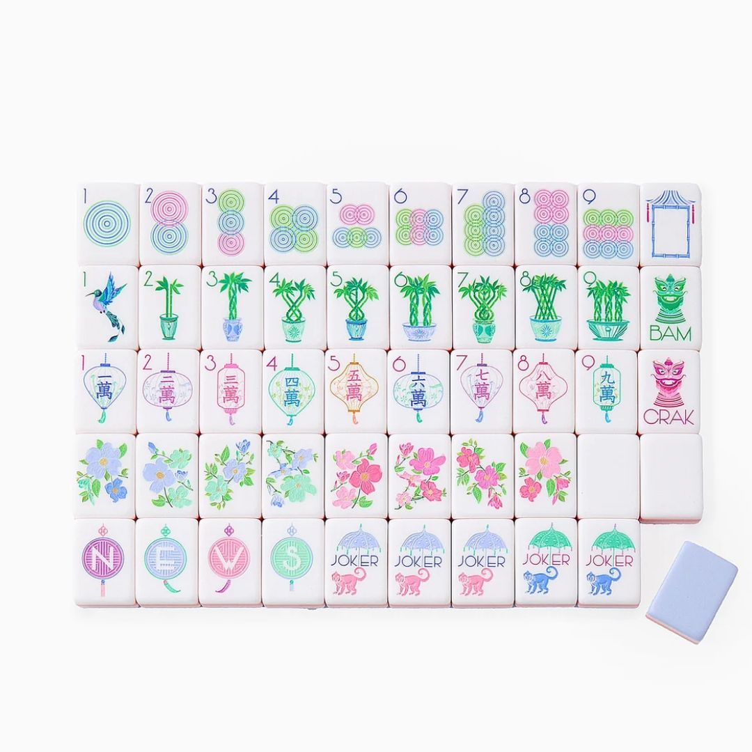 Close-up of white mahjong tiles with pastel pink and lavender sides, featuring colorful floral, bamboo, character, circle and joker designs arranged across a white surface.