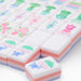 Close-up of white mahjong tiles with pastel pink and lavender sides, featuring colorful floral, bamboo, character, circle and joker designs arranged across a white surface.