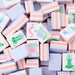 Close-up of white mahjong tiles with pastel pink and lavender sides, featuring colorful floral, bamboo, character, circle and joker designs arranged across a white surface.