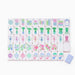 Close-up of white mahjong tiles with pastel pink and lavender sides, featuring colorful floral, bamboo, character, circle and joker designs arranged across a white surface.