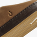 Close-up detail of a brown suede shoe upper with a dark brown leather stripe, contrast stitching, and a tan textured outsole.