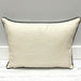 A rectangular lumbar throw pillow in textured cream fabric with dark charcoal gray piping, resting on a white wooden floor against a gray wall.