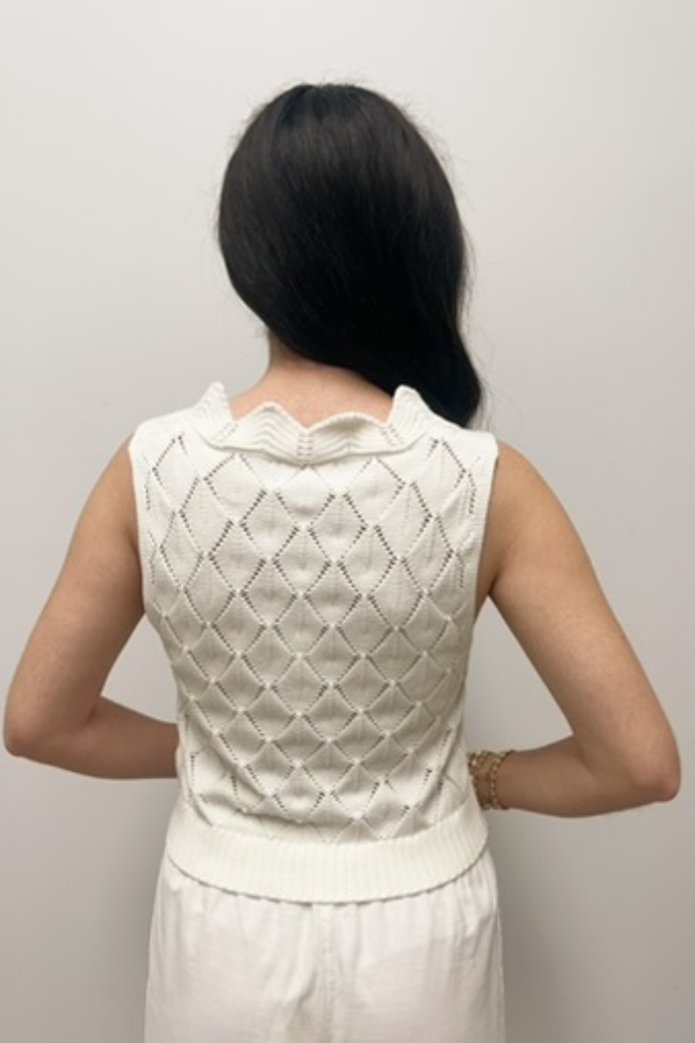 Person wearing a white sleeveless top with a textured pattern against a plain background