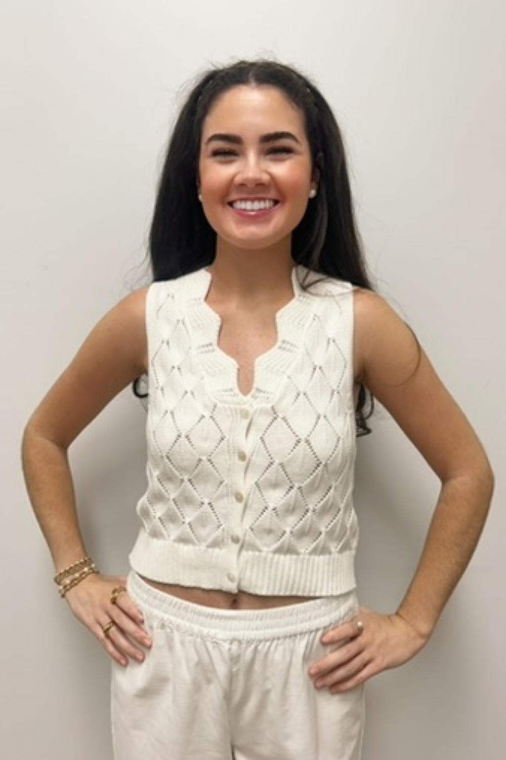 Woman wearing a white knitted vest and pants against a plain background