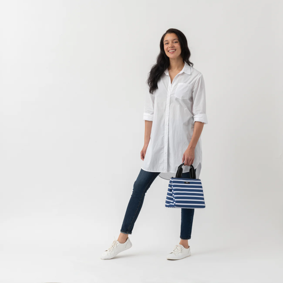 Woman wearing a white shirt and dark pants, holding a striped bag on a white background