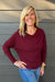Woman wearing Six Fifty Anywhere Top In Burgundy with jeans on a dark wood background.
