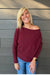 Woman wearing Six Fifty Anywhere Top In Burgundy with jeans on a dark wood background.