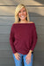 Woman wearing Six Fifty Anywhere Top In Burgundy with jeans on a dark wood background.