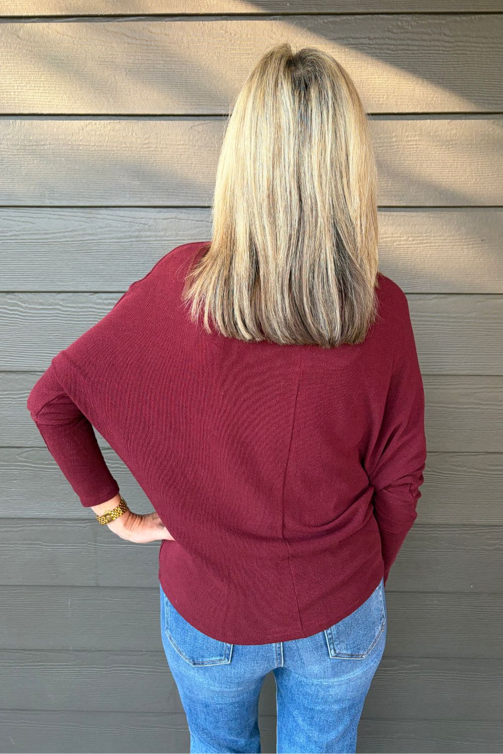 Woman wearing Six Fifty Anywhere Top In Burgundy with jeans on a dark wood background.