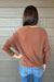 Woman wearing Six Fifty Anywhere Top In Chestnut with jeans on a dark wood background.