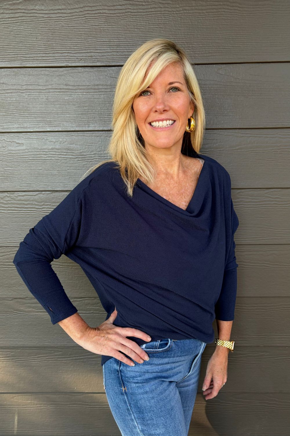 A woman wearing Six Fifty Anywhere Top In Navy with jeans on a dark wood background.