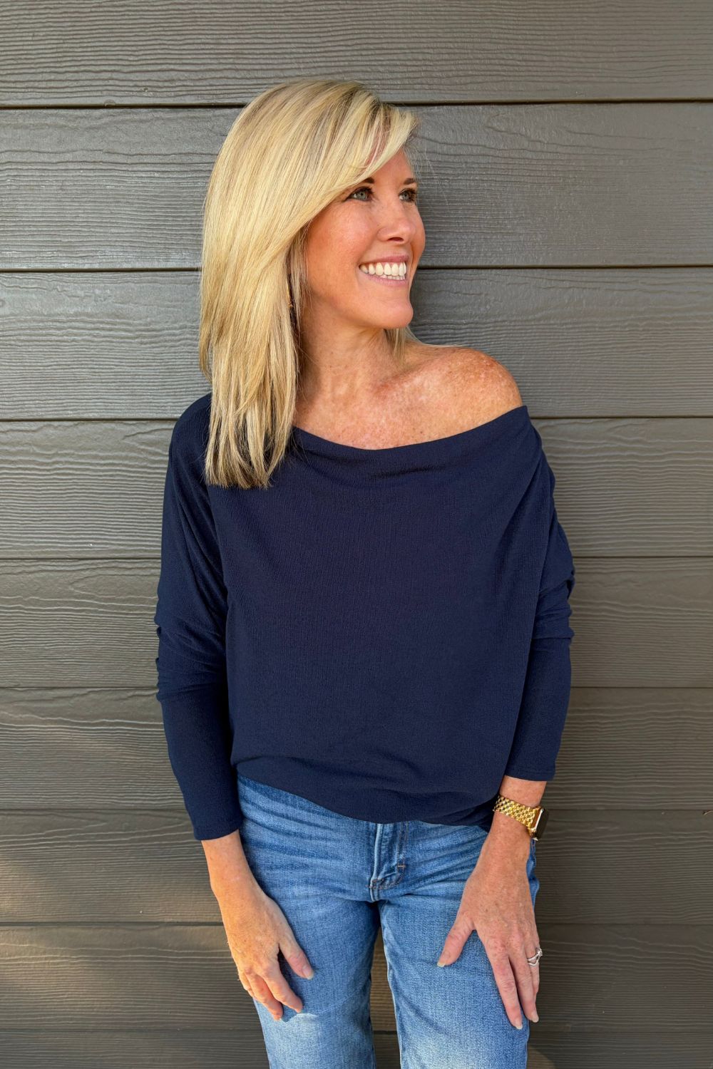 A woman wearing Six Fifty Anywhere Top In Navy with jeans on a dark wood background.