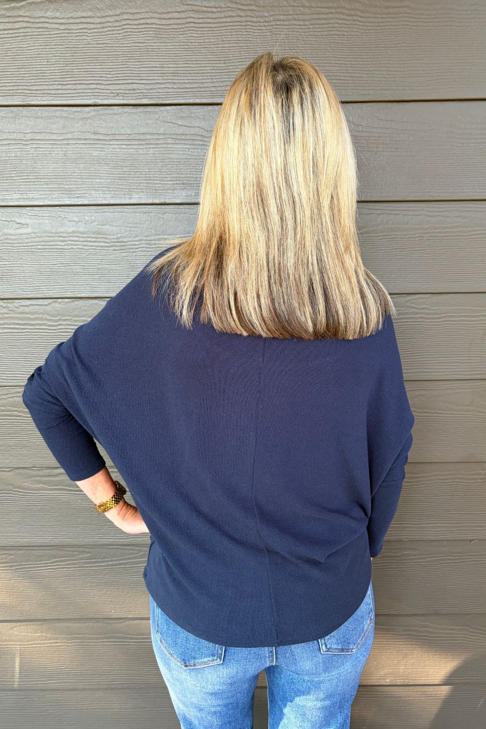 A woman wearing Six Fifty Anywhere Top In Navy with jeans on a dark wood background.