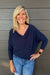 A woman wearing Six Fifty Anywhere Top In Navy with jeans on a dark wood background.