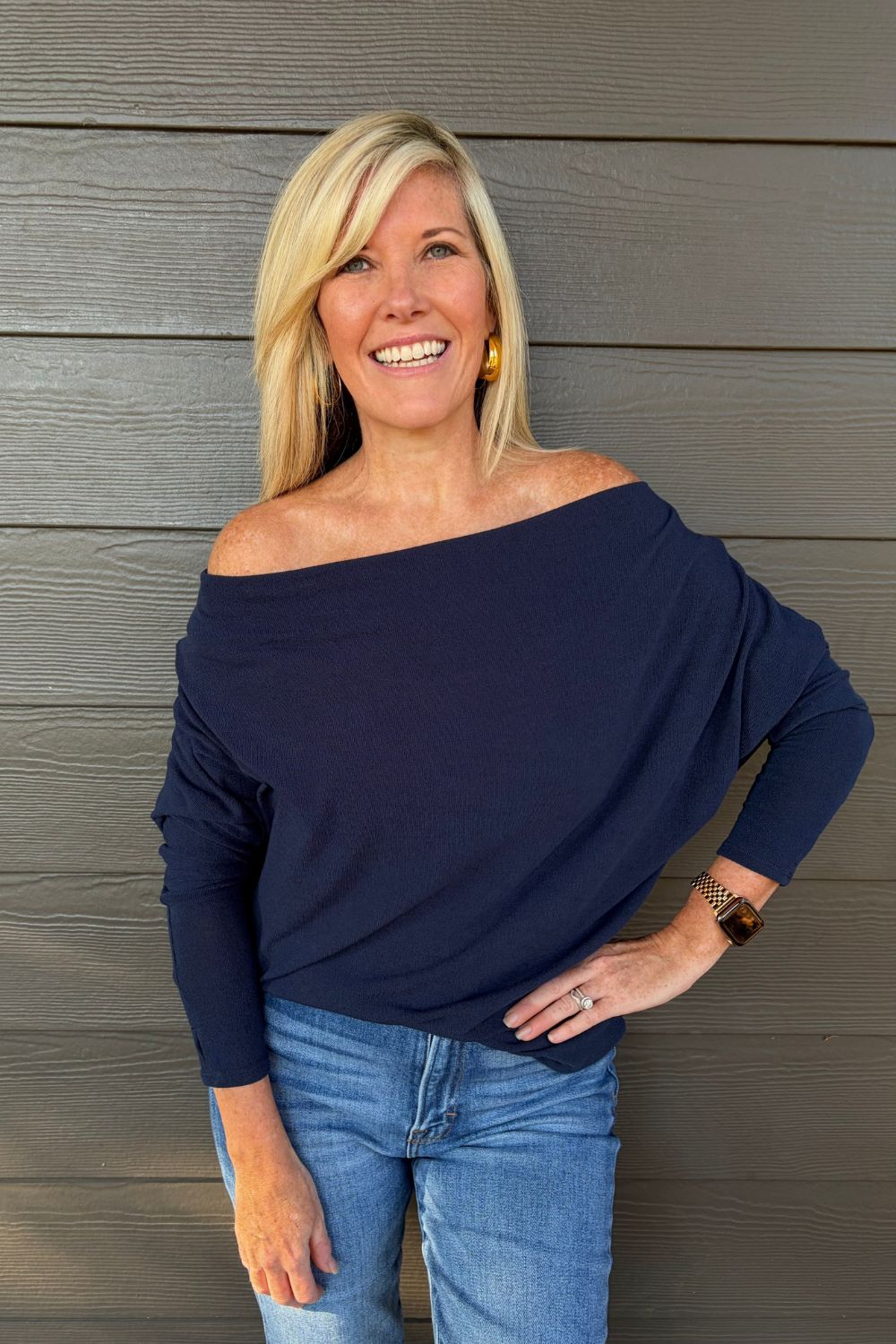 A woman wearing Six Fifty Anywhere Top In Navy with jeans on a dark wood background.