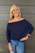 A woman wearing Six Fifty Anywhere Top In Navy with jeans on a dark wood background.