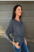Woman wearing Six Fifty Anywhere Top In Slate with blue jeans on a dark wood background.