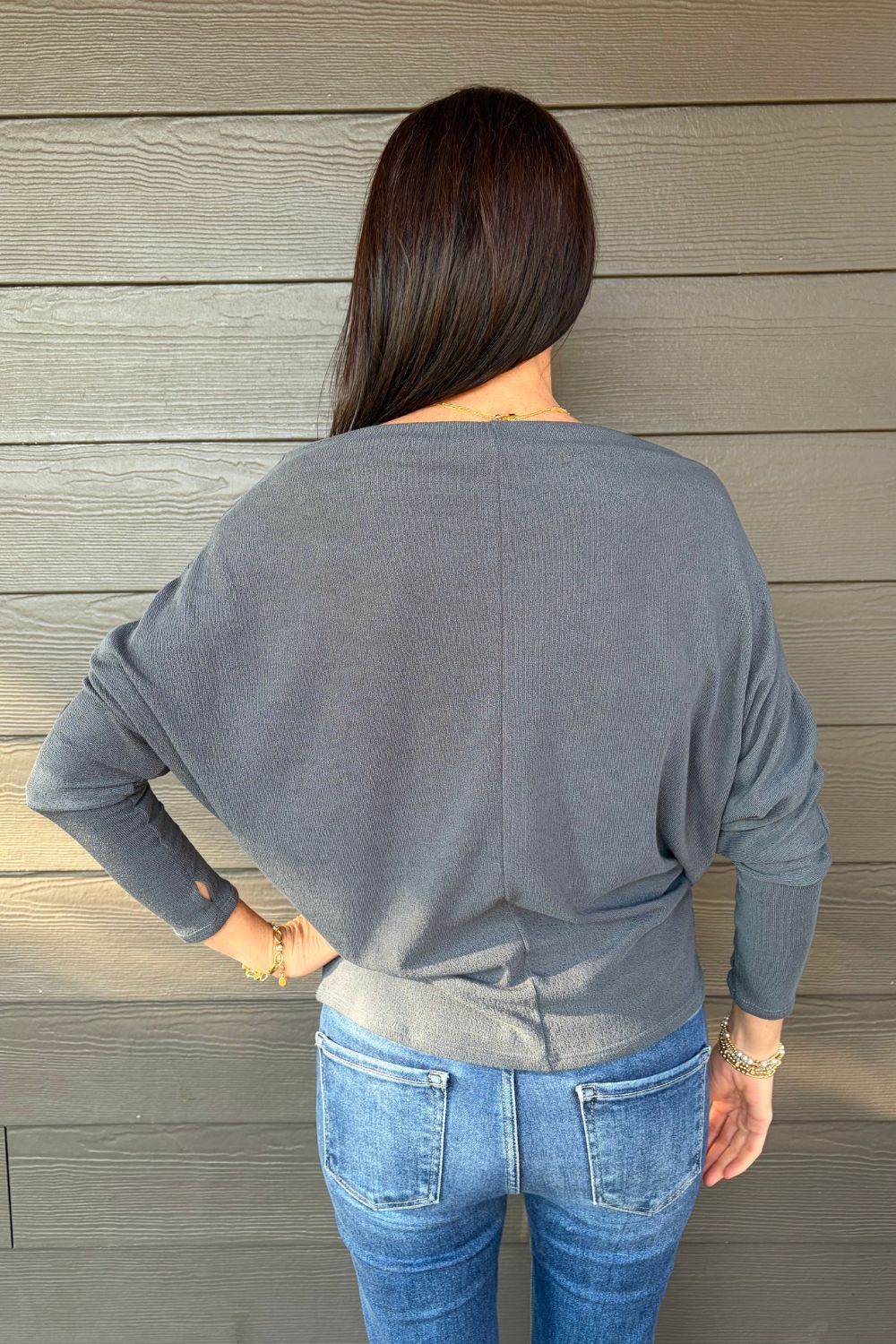 Woman wearing Six Fifty Anywhere Top In Slate with blue jeans on a dark wood background.