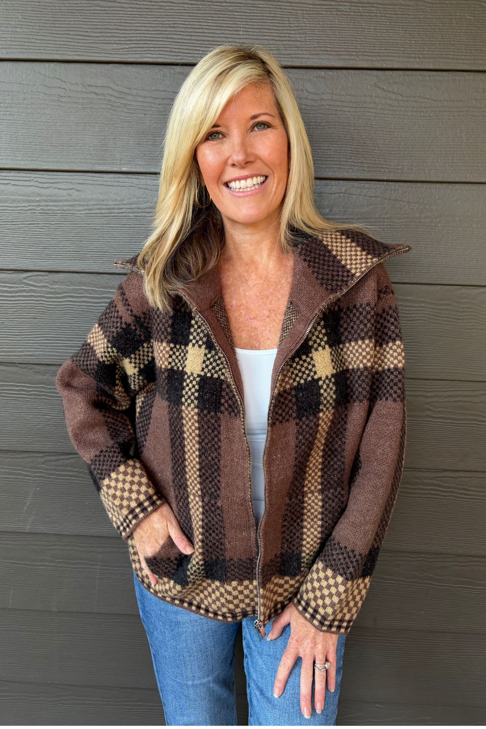 Woman wearing Six Fifty Cypress Plaid Zip Up In Brown with blue jeans on a dark wood background.