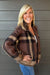 Woman wearing Six Fifty Cypress Plaid Zip Up In Brown with blue jeans on a dark wood background.