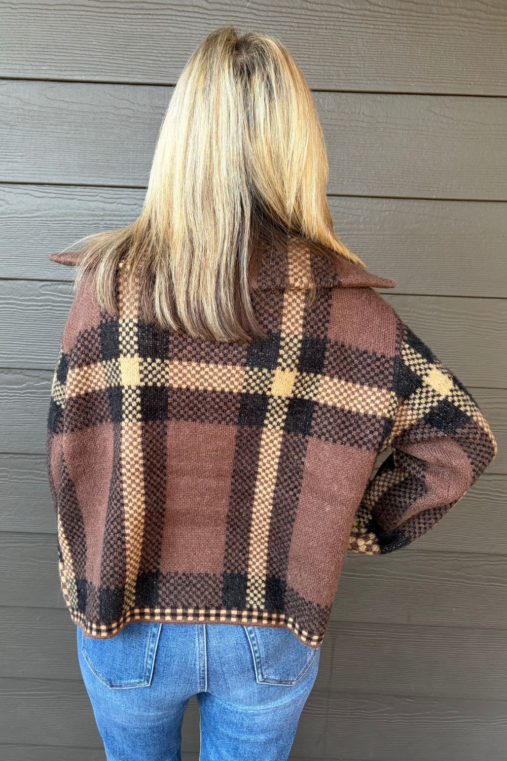 Woman wearing Six Fifty Cypress Plaid Zip Up In Brown with blue jeans on a dark wood background.