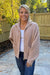 Woman wearing Softies Cable Knit Marshmallow Funnel Neck Double Zip Jacket Coco with blue jeans on standing on a patio.