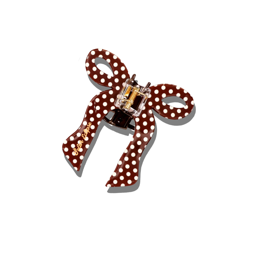 Brown bow-shaped hair clip with white polka dots on a white background