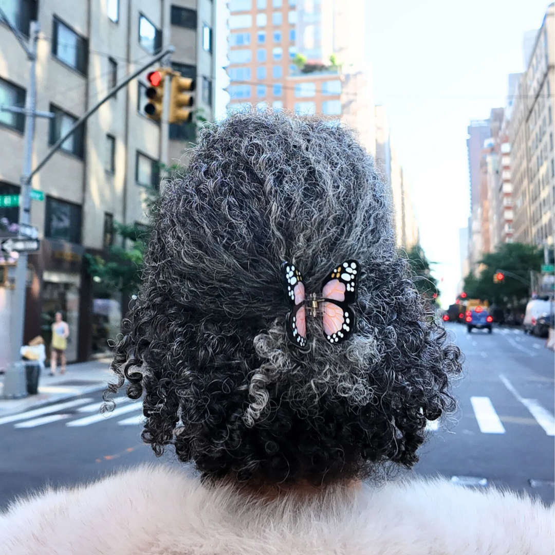 Close-up of a person with textured hair styled with butterfly accessories on a city street.