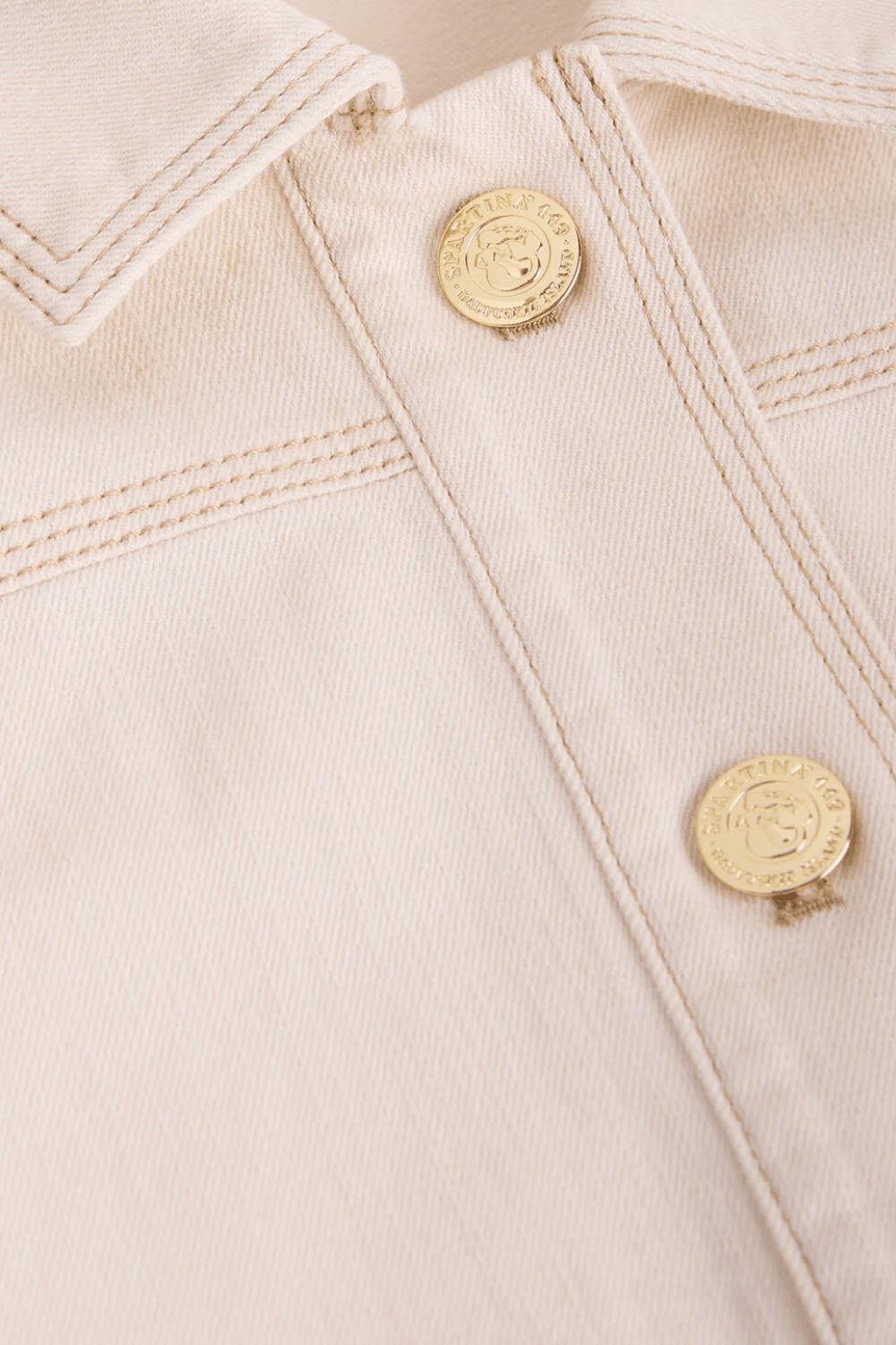 Close-up of a beige denim jacket with gold buttons on a matching beige background