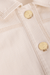 Close-up of a beige denim jacket with gold buttons on a matching beige background