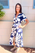 A woman wearing a navy blue and white floral print wrap maxi dress, standing outdoors against a beige stucco wall.