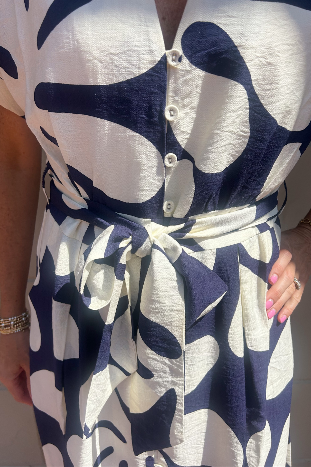 A close-up of a person wearing a short-sleeve button-front top or dress with an abstract navy and off-white pattern and a matching tie belt at the waist.